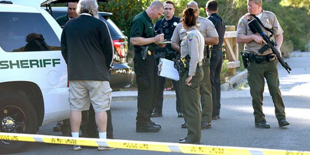 In this photo taken Wednesday, May 25, 2016, Marin County Sheriff and Novato police members gather at a command post to form a massive manhunt following at attack on two students in Novato, Calif. Attackers shot two students near a San Francisco Bay Area high school, killing one and sending another to a hospital in an incident that prompted the closing of the campus, authorities said Thursday. Both victims were students at Novato High School. (Robert Tong/Marin Independent Journal via AP)
