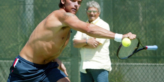 Mark Phillippoussis of Australia plays at the ball with the handle of his racket as his father Nick looks on during practice at the Sydney International Tennis Centre, Jan. 11, 2004.