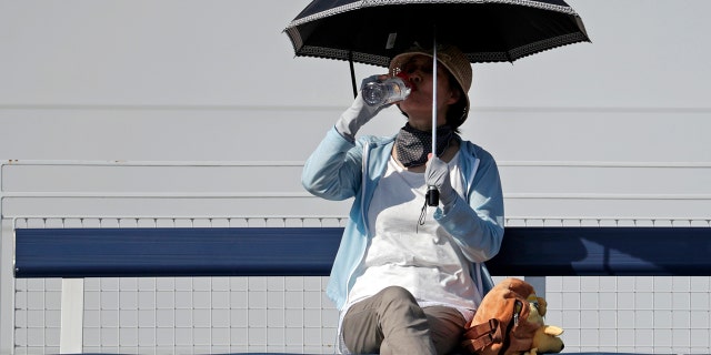 A fan shelters under an umbrella and sips a drink as she watches the match between Fabio Fognini, of Italy, and Michael Mmoh during the first round of the U.S. Open tennis tournament