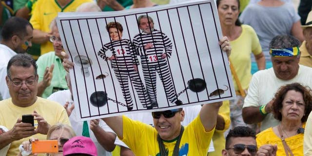 n this March 13, 2016 file photo, a demonstrator holds a poster with the photo of Brazilian president Dilma Rousseff and former President Luiz Inacio Lula da Silva in prison stripes during a protest on Copacabana beach in Rio de Janeiro, Brazil.