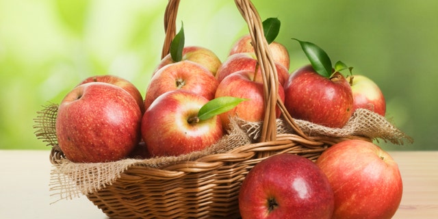 Jonagold apples in a basket on wooden table against garden background
