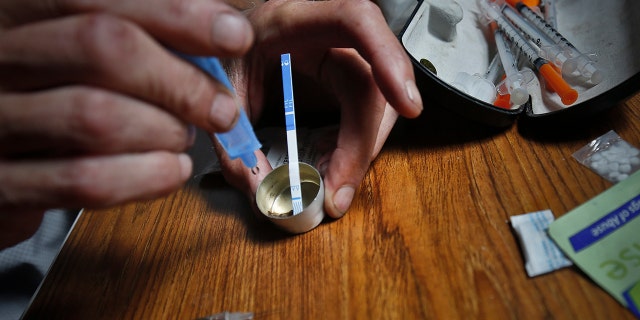 An addict prepares heroin, placing a fentanyl test strip into the mixing container to check for contamination.