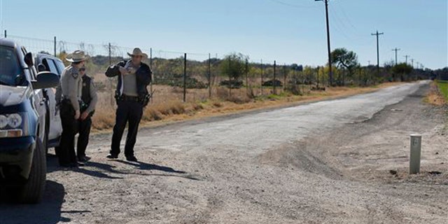 In this Saturday, Feb. 6, 2016 photo, Uvalde County Sheriffs Deputies guard the intersection to a neighborhood several miles outside of Uvalde, Texas.