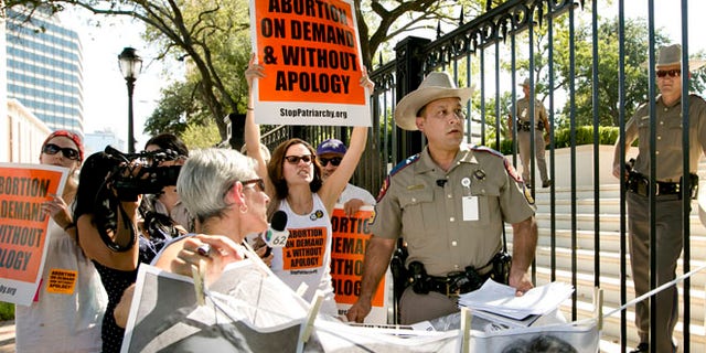 Aug 25, 2014: Pro-abortion rights activists chant slogans while a Texas Department of Public Safety trooper removes their signs from the gate of the Governor's Mansion in Austin, Texas.