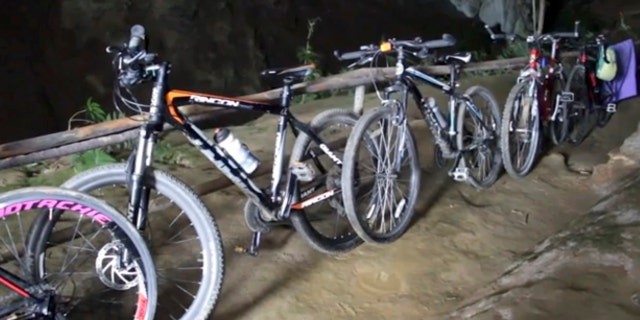 In this image made from video taken Sunday, June 24, 2018, bicycles left from a group of boys who went missing stand parked outside a deep cave in Chang Rai, northern Thailand.