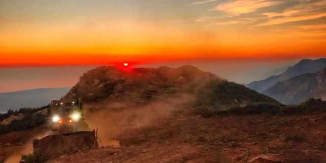 In this photo released by Santa Barbara County Fire Department, a dozer from the Santa Barbara County Fire Department clears a fire break across a canyon from atop Camino Cielo down to Gibraltar to make a stand should the fire move in that direction, Wednesday, Dec. 13, 2017, in the Santa Ynez Mountains area of Santa Barbara, Calif.