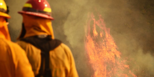 In this photo provided by the Santa Barbara County Fire Department, firefighters keep an eye on flames as pockets of unburned vegetation flare up off Bella Vista Dr. in Montecito, Calif., Wednesday, Dec. 13, 2017.