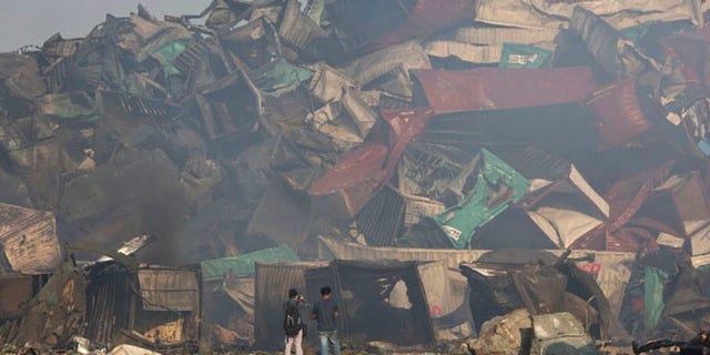 Photographers walk near the deformed remains of containers after an explosion at a warehouse in northeastern China's Tianjin municipality, Thursday, Aug. 13, 2015. Huge, fiery blasts at a warehouse for hazardous chemicals killing many people and turned nearby buildings into skeletal shells in the Chinese port of Tianjin, raising questions Thursday about whether the materials had been properly stored. (AP Photo/Ng Han Guan)