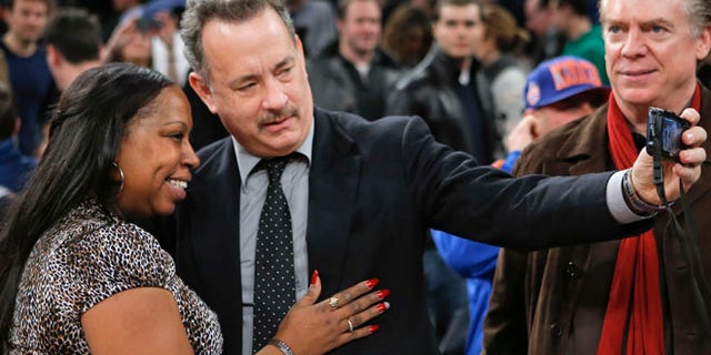 Actor Tom Hanks (C) tries to take a picture with a fan after the New York Knicks played the Los Angeles Clippers in their NBA basketball game at Madison Square Garden in New York, February 10, 2013. Actor Christopher McDonald (R) watches. REUTERS/Ray Stubblebine (UNITED STATES - Tags: SPORT BASKETBALL) - RTR3DLLE