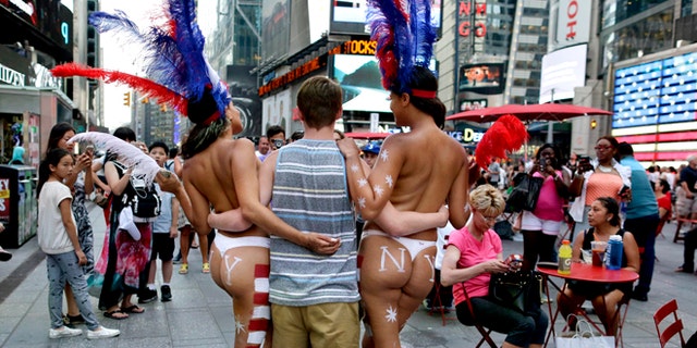 July 28, 2015: a tourist poses for a photo with two women clad in thongs and body paint in Times Square, in New York. (AP)