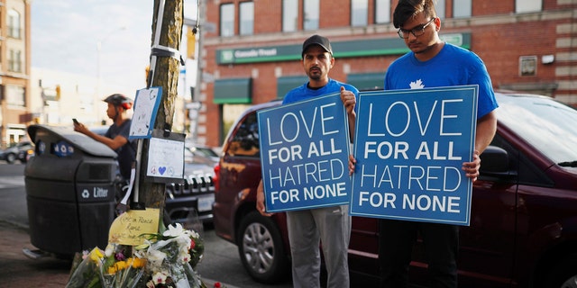 People hold signs at a memorial remembering the victims of Sunday's shooting in Toronto.