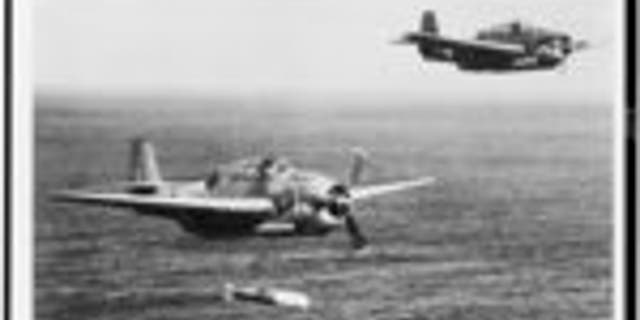 Two U.S. Navy Grumman Avenger torpedo-bombers in flight over the ocean, one having just released a torpedo