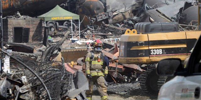 July 6, 2013: This file photo shows a worker, wearing protective gear moving though the wreckage of the oil train derailment and explosion in in Lac-Megantic, Quebec.