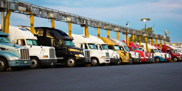 Several diesel semi-trucks lined up for fueling at a truck stop blue sky white clouds