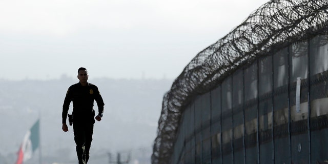 Border Patrol agent Eduardo Olmos walks near the secondary fence separating Tijuana, Mexico.