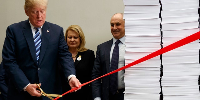 President Donald Trump cuts a ribbon during an event on federal regulations in the Roosevelt Room of the White House, Thursday, Dec. 14, 2017, in Washington. "Let's cut the red tape, let's set free our dreams," Trump said as he symbolically cut a ribbon on stacks of paper representing the size of the regulatory code. (AP Photo/Evan Vucci)