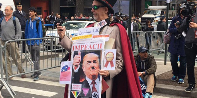 A man dressed in a top hat and cape wears a picture of President Trump with an Adolf Hitler-style mustache.