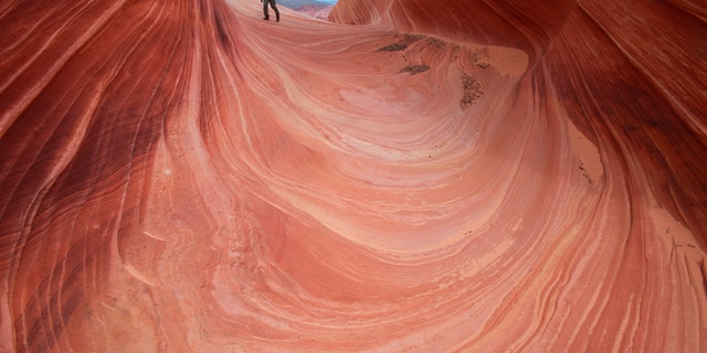 In this May 28, 2013, file photo, a hiker walks on a rock formation known as The Wave in the Vermilion Cliffs National Monument in Arizona.