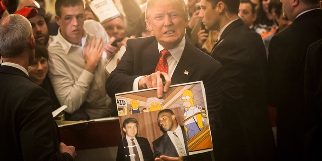 In this Jan. 29, 2016, file photo, Republican presidential candidate Donald Trump holds depictions of himself on, "The Simpsons" and a photo with boxer Mike Tyson, given to him by an attendee during a campaign stop at the Radisson Hotel in Nashua, N.H. "The Simpsons" released a short online clip on April 26, 2017, mocking President Donald Trump ahead of his 100th day in office.