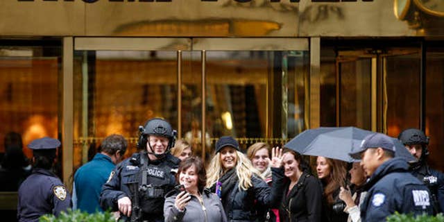 Passersby stop for a selfie with a heavily-armed New York City police officer at the main, Fifth Avenue entrance to Trump Tower, Tuesday, Nov. 15, 2016, in New York. For nearly the entire week since he became president-elect, Donald Trump has been holed up in the tower, his gilded New York skyscraper.