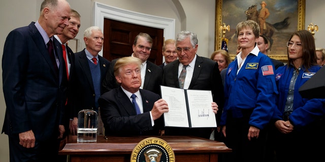 President Donald Trump holds up a policy directive to send American astronauts back to the moon, and eventually Mars, in the Roosevelt Room of the White House, Monday, Dec. 11, 2017, in Washington. (AP Photo/Evan Vucci)