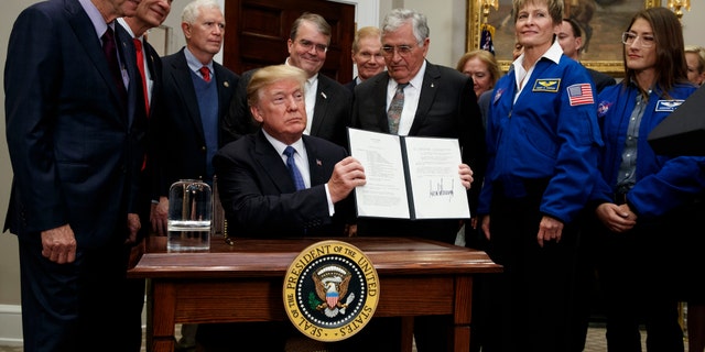 President Donald Trump holds up a policy directive to send American astronauts back to the moon, and eventually Mars, in the Roosevelt Room of the White House, Monday, Dec. 11, 2017, in Washington. (AP Photo/Evan Vucci)