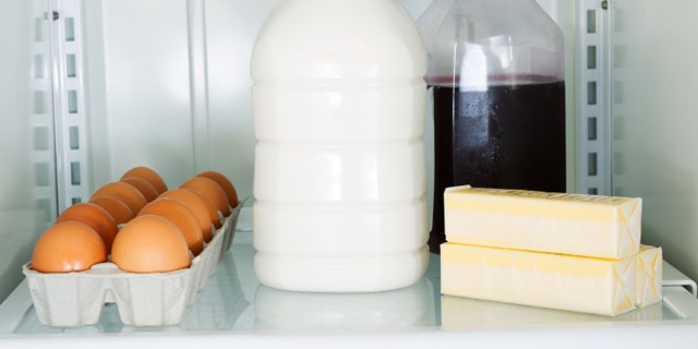 Horizontal photo of milk, eggs, butter and juice on glass shelf inside of refrigerator