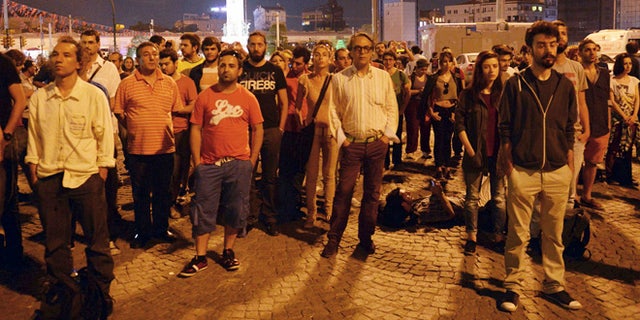 June 18, 2013: Erdem Gunduz, left, and dozens of people stand silently on Taksim Square in Istanbul, Turkey. After weeks of confrontation with police, sometimes violent, Turkish protesters are using a new form of resistance: standing silently. The development started late Monday when a solitary man began standing in passive defiance against Prime Minister Recep Tayyip Erdogan's authority at Istanbul's central Taksim Square.