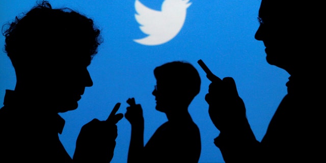 People holding mobile phones are silhouetted against a backdrop projected with the Twitter logo.