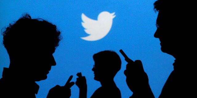 People holding mobile phones are silhouetted against a backdrop projected with the Twitter logo.