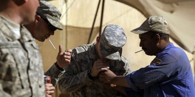 In this photo taken Wednesday, March 16, 2011, an Iraqi Army soldier, right, lights a cigarette for U.S. Army Sgt. Brett Lester, center, of Riverside, Calif. , from D Co. , 1st Battalion, 18th Infantry Regiment, 2nd Brigade, 1st Infantry Division, during training on M1A1 Abrams tanks at Camp Taji, north of Baghdad, Iraq. (AP)