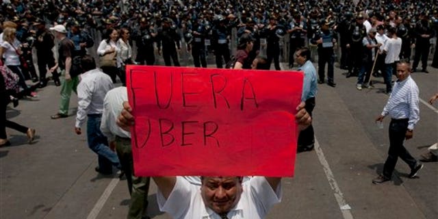 A man holds a sign the reads in Spanish "Uber Out" in front of a phalanx of riot police as thousands of taxi drivers blocked the main streets in Mexico City, Monday, May 25, 2015. The Mexican taxi drivers' union called for a protest against unlicensed and UBER taxis working in Mexico City. (AP Photo/Marco Ugarte)