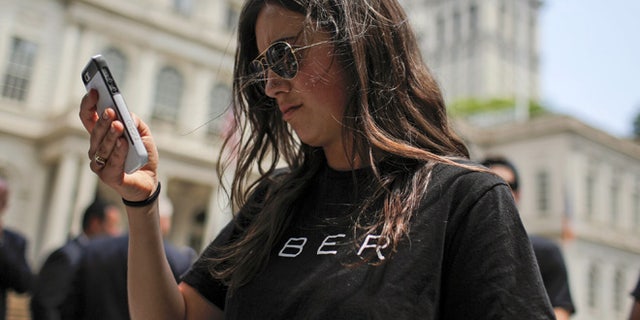 FILE: A woman wearing a Uber T-shirt checks her phone while Uber riders and driver-partners take part in a rally on the steps of New York City Hall.