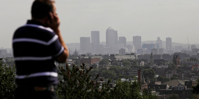 FILE In this Friday, Sept. 23, 2011 file photo a man talks on a mobile phone as the hi-rise buildings of the banks based in the Canary Wharf business district are seen in the distance from Parliament Hill on Hampstead Heath in London.
