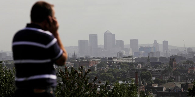 FILE In this Friday, Sept. 23, 2011 file photo a man talks on a mobile phone as the hi-rise buildings of the banks based in the Canary Wharf business district are seen in the distance from Parliament Hill on Hampstead Heath in London.