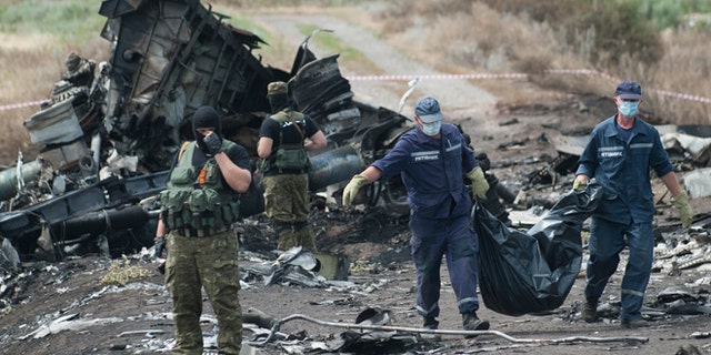 July 20, 2014: Ukrainian Emergency workers carry a stretcher with a victim's body in a bag as pro-Russian fighters stand in guard at the crash site of Malaysia Airlines Flight 17 near the village of Hrabove, eastern Ukraine.