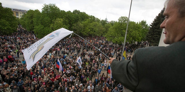 April 29, 2014: A Pro-Russian activist waves a Donbas Republic flag over a crowd celebrating the capture of an administration building in the center of Luhansk, Ukraine, one of the largest cities in Ukraine's troubled east, as demonstrators demand greater autonomy for Ukraine's regions.