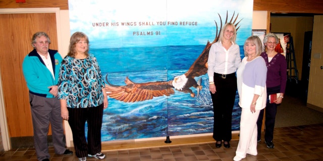 Fred Lewallen, left, Nancy Cupp, Mayor Lydia Mihalik, Judi Herrin, and Cathy Schock in front of the "Under His Wings" mural in Findlay's municipal building.