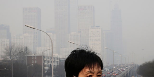 In this Dec. 20, 2015 file photo, a woman wearing a mask for protection against pollution walks on a pedestrian overhead bridge as office buildings are shrouded with smog in Beijing.