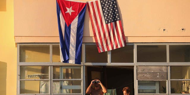 HAVANA, CUBA - AUGUST 14: Cubans look out their window across the street from the newly reopened U.S. Embassy in hopes of watching the flag-raising ceremony August 14, 2015 in Havana, Cuba. The first American secretary of state to visit Cuba since 1945, Secretary of State John Kerry visited the reopened embassy, a symbolic act after the the two former Cold War enemies reestablished diplomatic relations in July. (Photo by Chip Somodevilla/Getty Images)