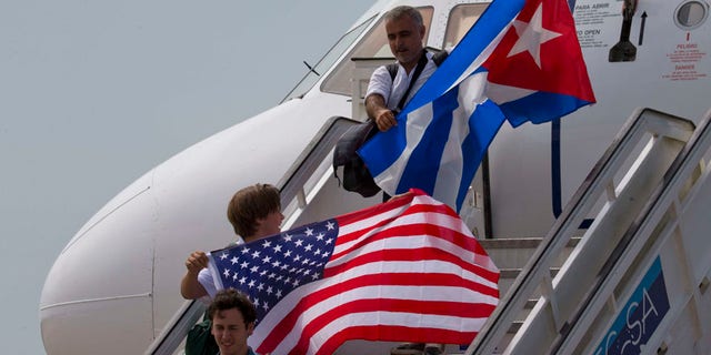 FILE- In this Aug. 31, 2016 file photo, two passengers deplane from JetBlue flight 387 waving a United States, and Cuban national flag, in Santa Clara. As President Donald Trump is expected to announce a reversal on the U.S. Cuba policy on Friday, June 16, 2017, Cubans are bracing for the worst. Across the island, people of all ages, professions and political beliefs expect rising tensions, fewer American visitors and a harder time seeing relatives in the U.S.(AP Photo/Ramon Espinosa, File)