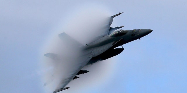 A F18 Super Hornet creates a vapor cone as it flies at a transonic speed while doing a flyby of the USS Eisenhower off the coast of Virginia