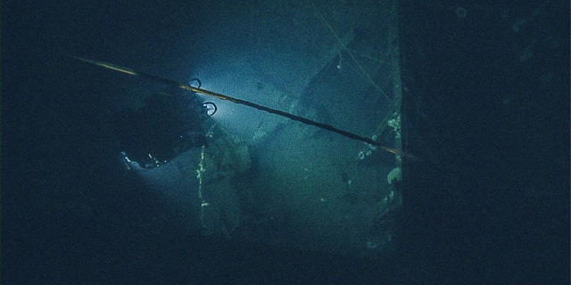 Lights from ROV Hercules illuminate deck of USS Independence, with view of tether running from ROV Hercules to ROV Argus (OET/Nautilus Live).
