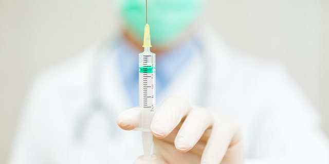 Doctor is holding an injection with needle with focus on injection