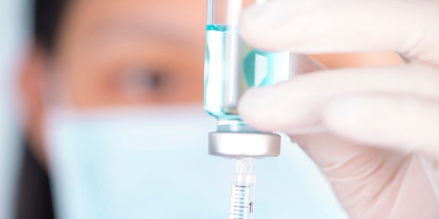 Closed up Nurse fills syringe from injection vial on white