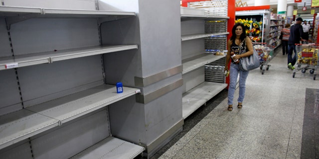 A woman walks past an empty section where toilet paper should be on display in a super market in Caracas.