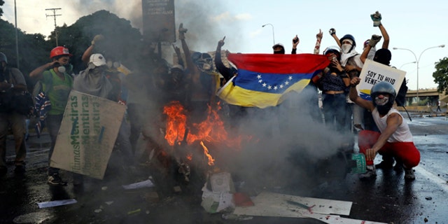 Opposition supporters hold a Venezuelan national flag in front of a burning riot security force motorcycle during clashes at a rally against Venezuelan President Nicolas Maduro's government in Caracas, Venezuela June 22, 2017. REUTERS/Carlos Garcia Rawlins - RTS189Z3
