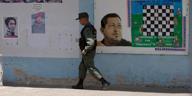 A Bolivarian National Guards officer walks near images of the late Venezuelan President Hugo Chavez and Independence hero Simon Bolivar, left, at a poll station in Caracas, Venezuela, Sunday, May 17, 2015. Venezuelans are voting to select the opposition leaders who will run against the ruling socialist partyâs candidates in upcoming legislative elections thought to be government criticsâ first chance at an electoral victory in years. (AP Photo/Fernando Llano)