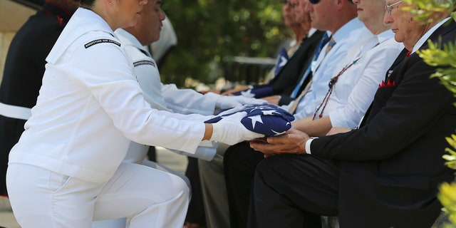 Navy Reservist Second Class Petty Officer Linda Villalobos presents a folded U.S. Flag to an official as Fort Sam Houston National Cemetery and the Missing In America Project conduct a military burial service for the cremated remains of eight unclaimed veteran in San Antonio.