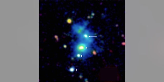 This image shows a rare view of four quasars, indicated by white arrows, found together by astronomers using the Keck Observatory in Hawaii. The bright galactic nuclei are embedded in a giant nebula of cool, dense gas visible in the image as a